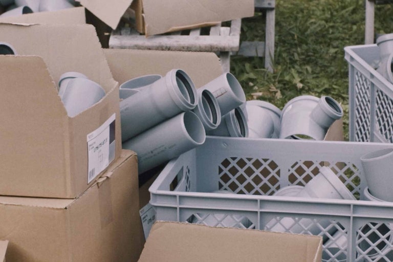 Šedé odpadní trubky a tvarovky v kartonech a plastové nádobě.