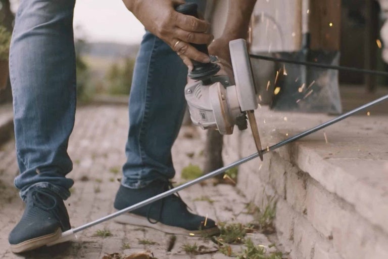 Osoba řeže tyč úhlovou bruskou.