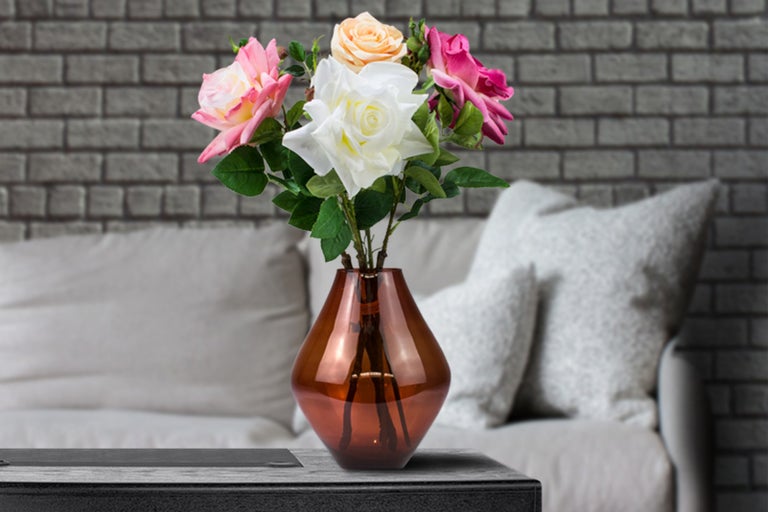 Kytice růží ve váze na stole před pohovkou a cihlovou zdí