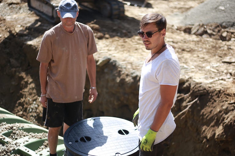 Dva stavební dělníci instalují žumpu na staveništi.