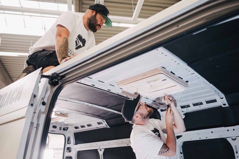 Dva muži montují střešní okno do dodávky.