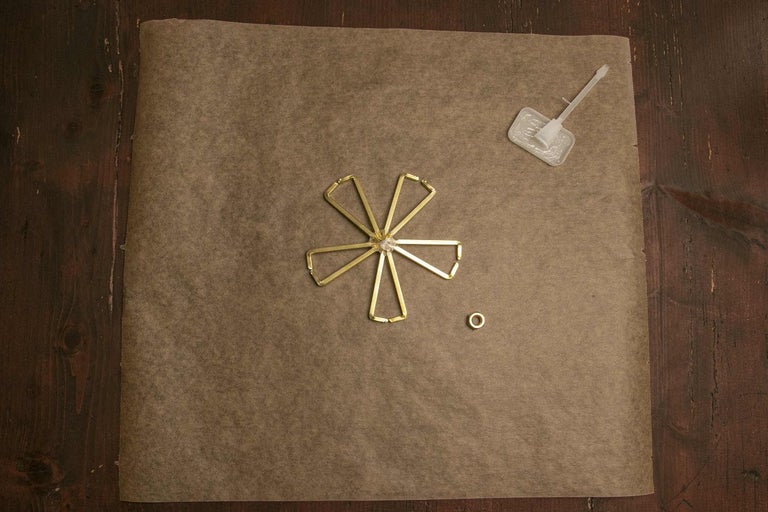 Mosazné díly ve tvaru květiny, nýt a lepidlo na hnědém pozadí.