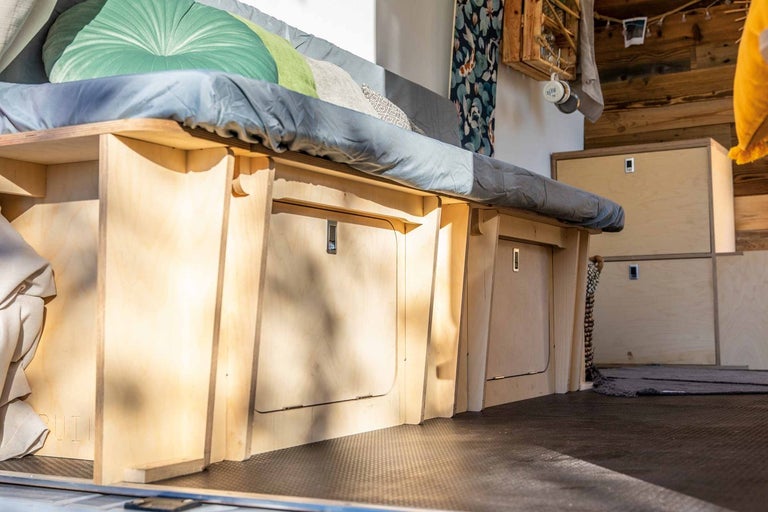 Interiér vozidla s dřevěnou postelí a úložnými řešeními