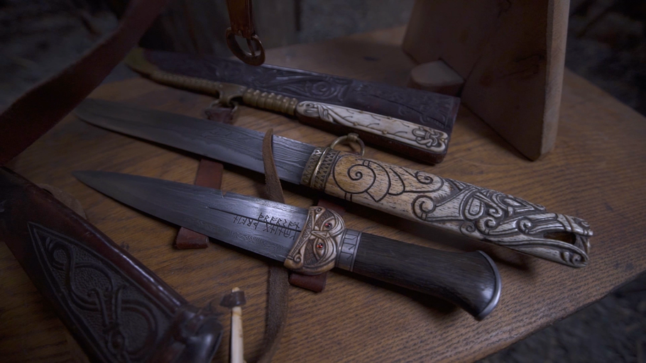 Tři nože se zdobnými rukojeťmi a pochvami na dřevěném stole.