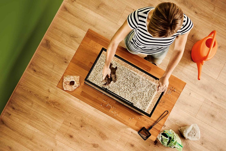 Žena zdobí akvárium štěrkem a dekoracemi