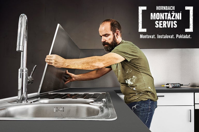 Řemeslník montuje kuchyňskou zástěnu nad dřezem, v pozadí logo montážního servisu Hornbach