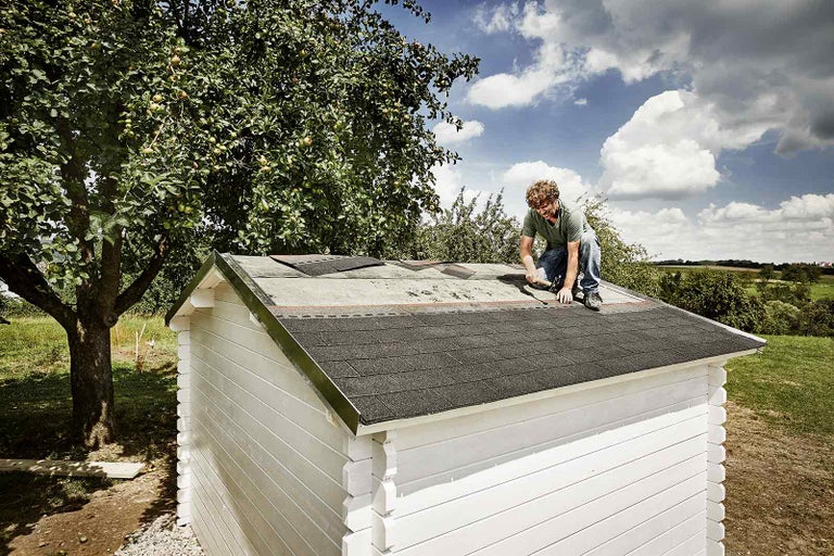 Muž pokládá střešní lepenku na střechu zahradního domku.
