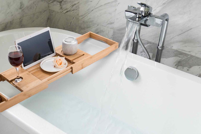Scéna naplněné vany s dřevěnou policí na vanu, tabletem, sklenicí vína, miskou s květinou a svíčkou