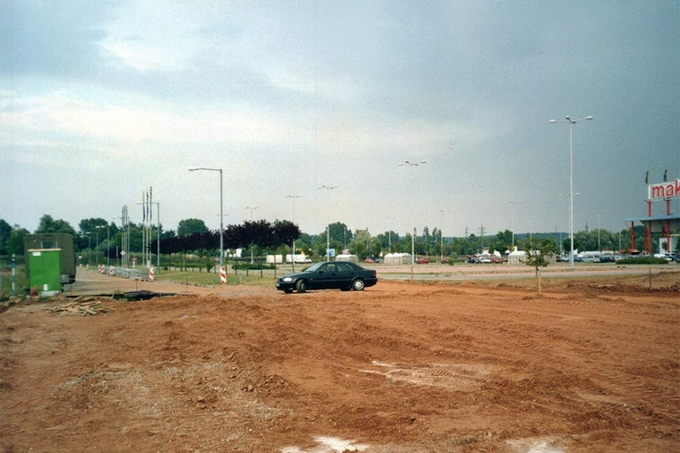 Nezastavěná plocha s zaparkovaným autem a pouličními lampami.