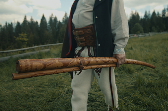 Muž v tradičním oděvu drží trembitu, dlouhý dřevěný alpský roh