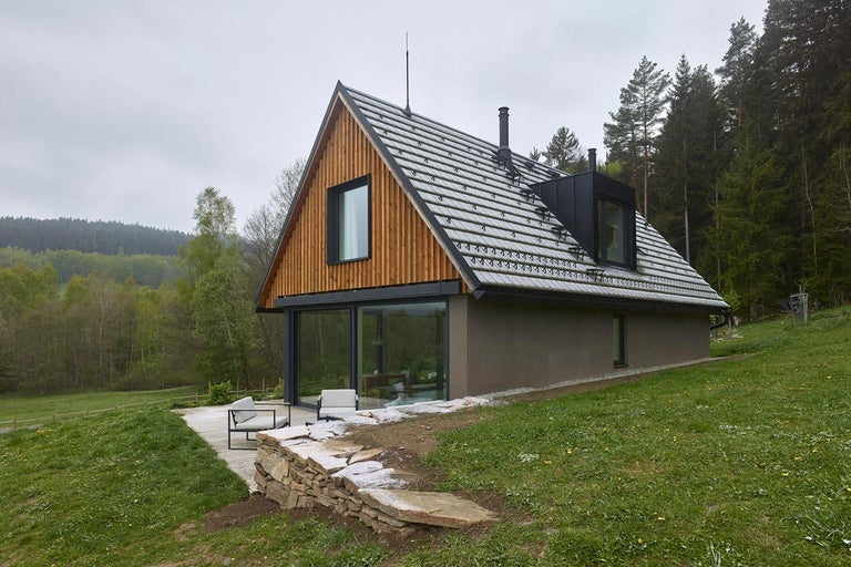 Vnější pohled na moderní dům se sedlovou střechou, dřevěným obkladem a velkými okny.
