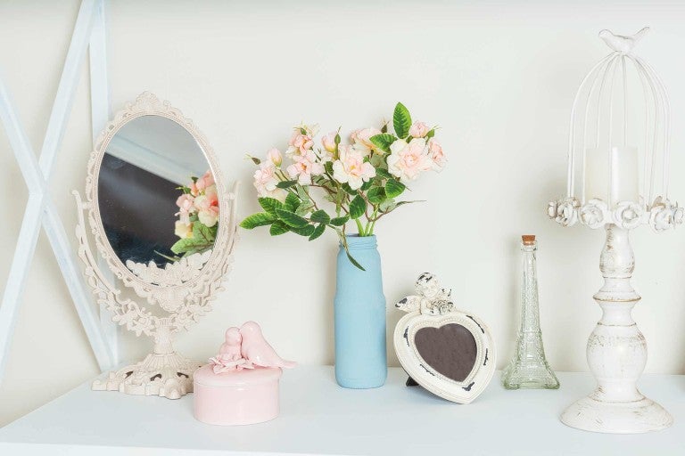 Dekorativní uspořádání se zrcadlem, květinami, svícnem a rámečkem na fotografie na světlém povrchu.