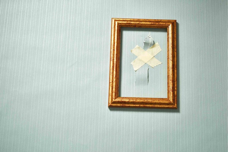 Zlatý rám obrazu visí s lepicí páskou na tapetě