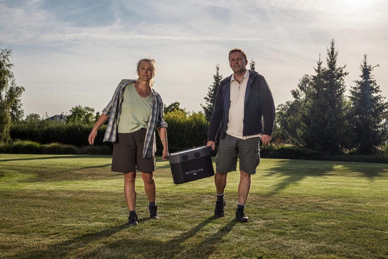 Dva lidé nesou přenosnou elektrárnu Ecoflow na trávníku.