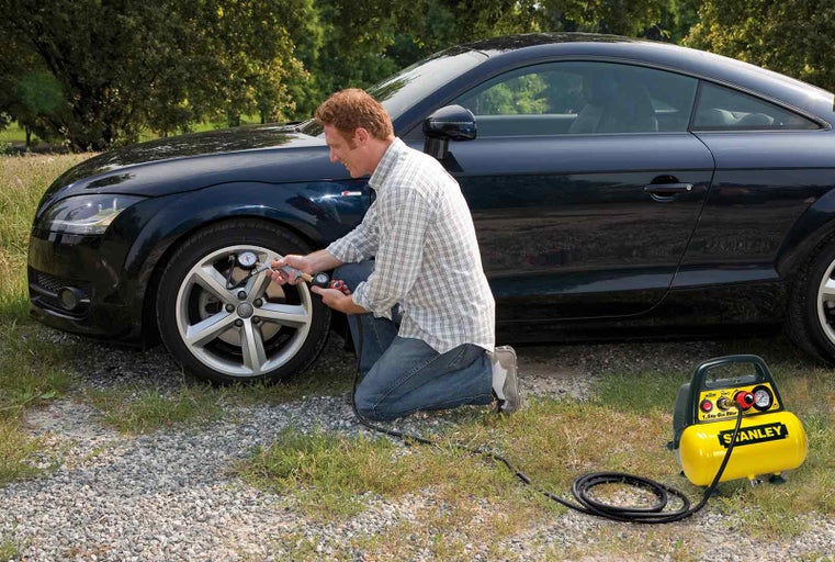 Muž kontroluje tlak v pneumatikách žlutým kompresorem Stanley u auta