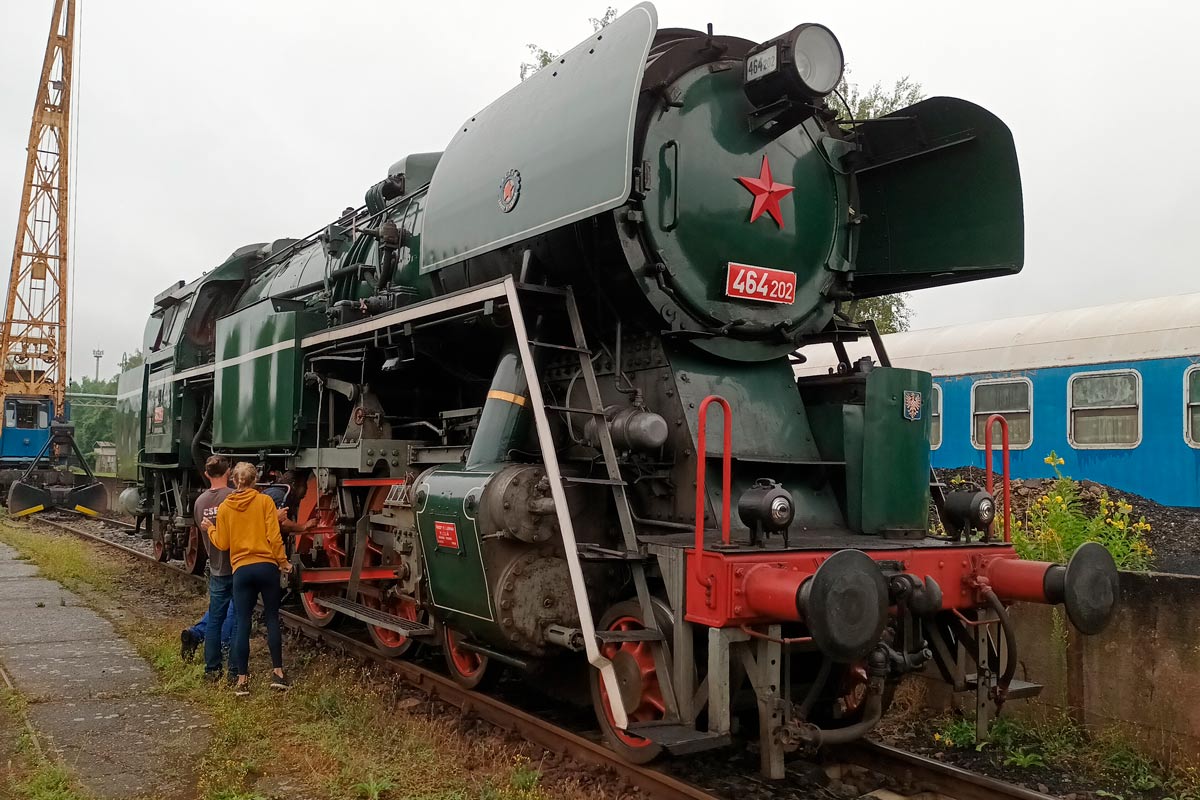 Zelená parní lokomotiva s červenou hvězdou a číslem 464 202 stojí na železniční trati.