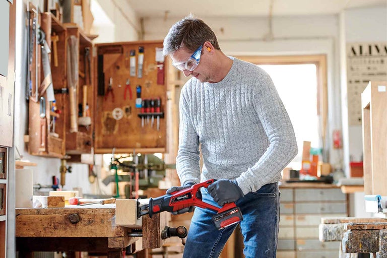 Muž pracuje s akumulátorovou ocaskou na obrobku v dílně.