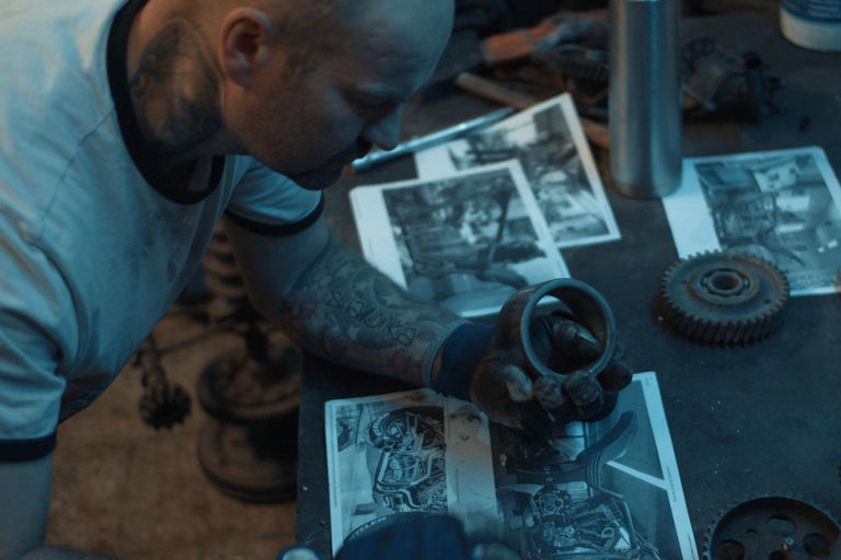 Muž v dílně si prohlíží motocyklové díly a výkresy.