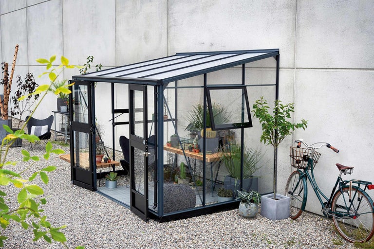 Skleněný skleník s rostlinami, stolem, židlí a kolem na zahradě.