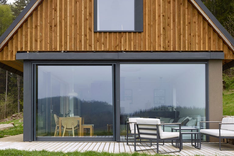Moderní dům s dřevěnou fasádou, velkými okny a terasovým nábytkem