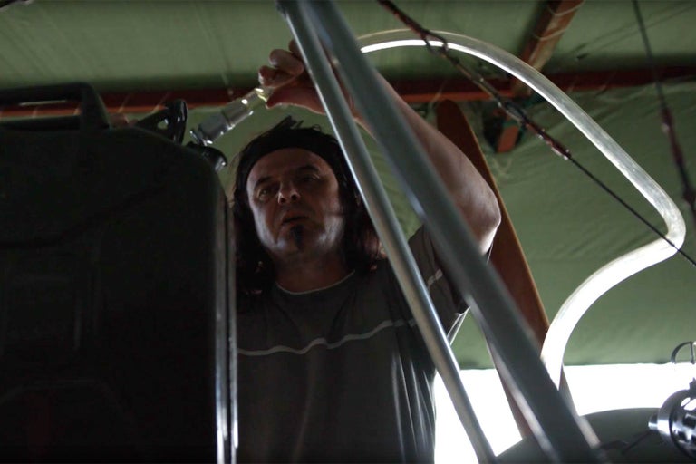 Muž plní palivový kanystr průhlednou hadicí