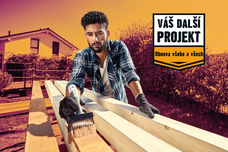 Muž natírá dřevěné lamely venku štětcem, v pozadí je dům.