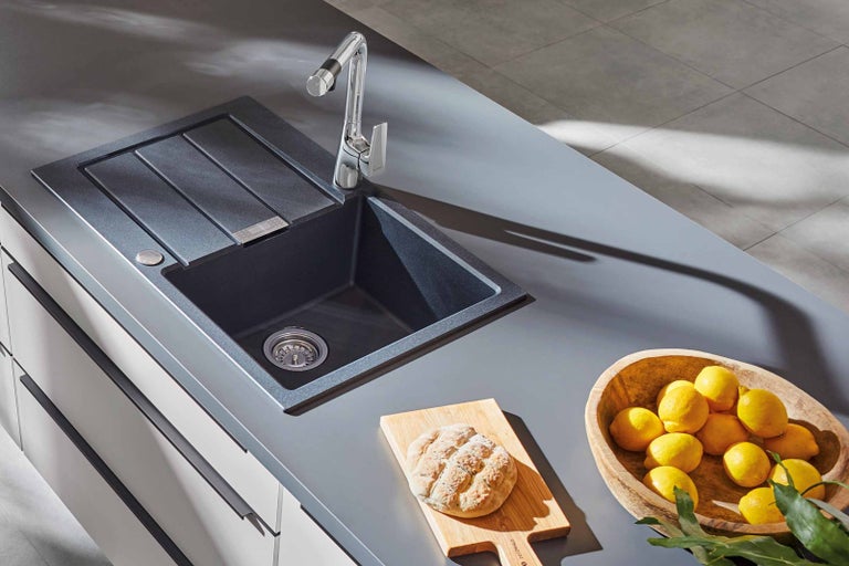 Žulový kuchyňský dřez s odkapávací plochou a baterií na pracovní desce s chlebem a citrony