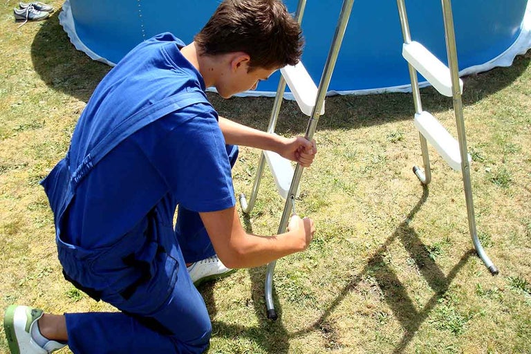 Muž montuje bazénový žebřík poblíž bazénu.