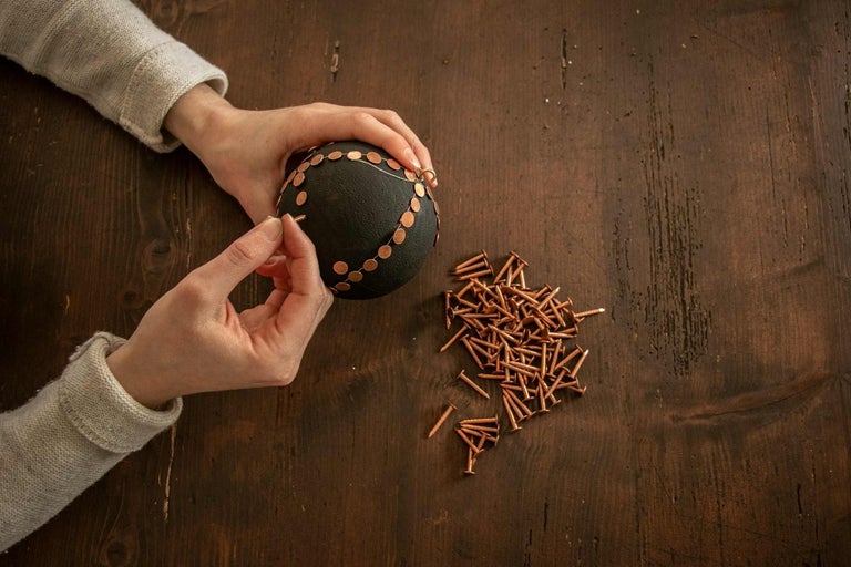 Osoba připevňuje zdobené prvky hřebíky k kouli.