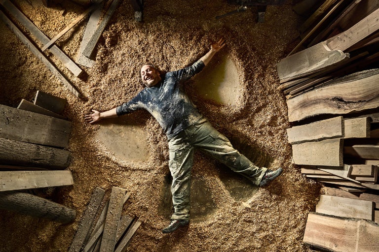 Muž leží na zemi obklopen dřevem a pilinami