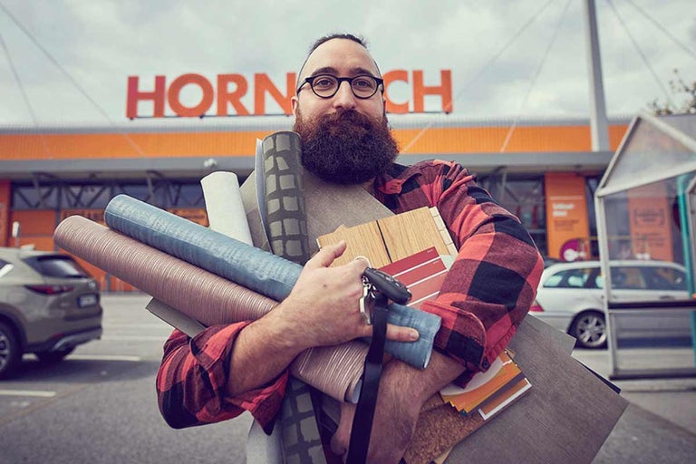 Muž před hobbymarketem Hornbach nese stavební materiály a vzorky barev.
