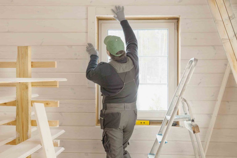 Muž montuje okenní rám v jasné místnosti s dřevěným obložením