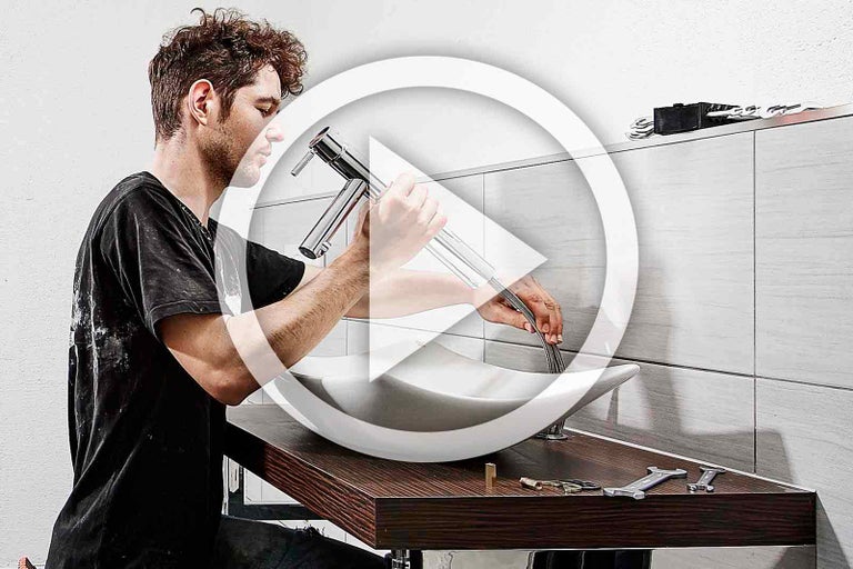 Muž instaluje vodovodní kohoutek do umyvadla v koupelně.