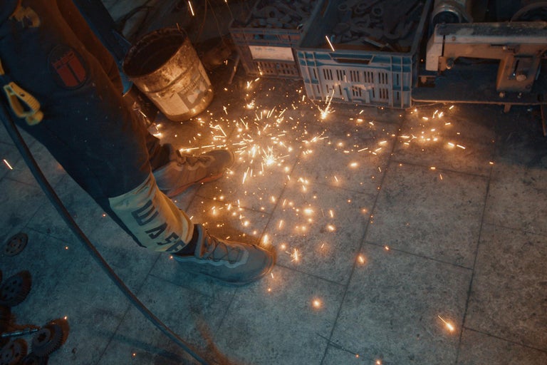 Jiskry při obrábění kovu s pracovním oděvem a bezpečnostní obuví.