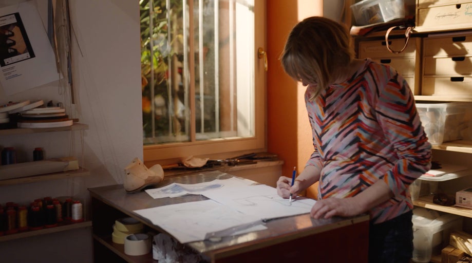 Žena kreslí návrh boty na papír v dílně.