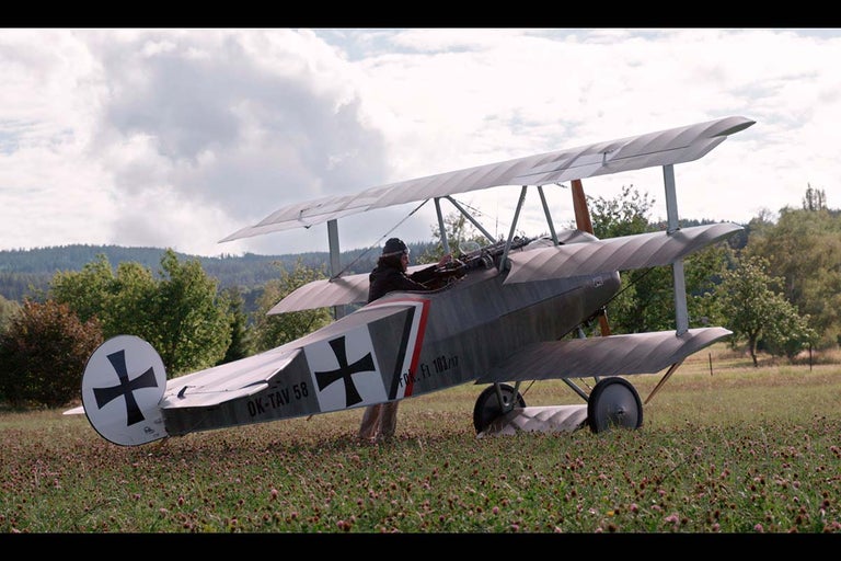Dvouplošníkové letadlo s pilotem na louce