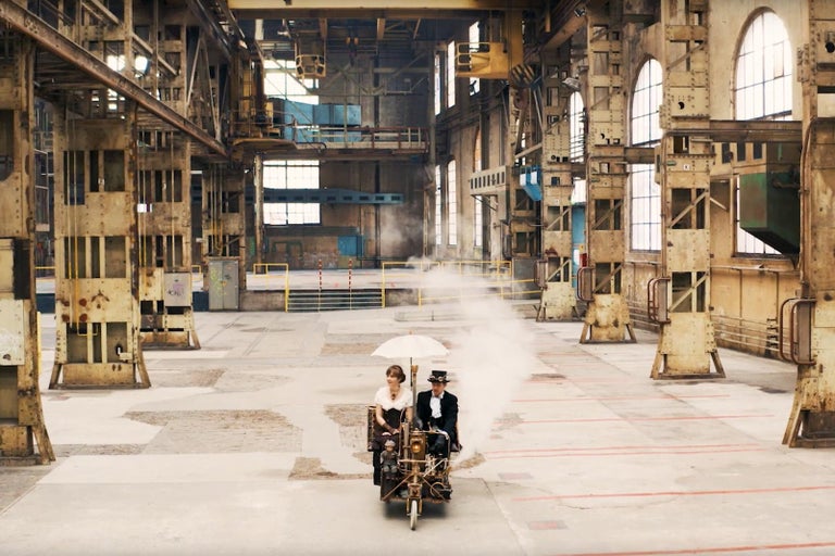 Scéna v tovární hale s párem na neobvyklém vozidle