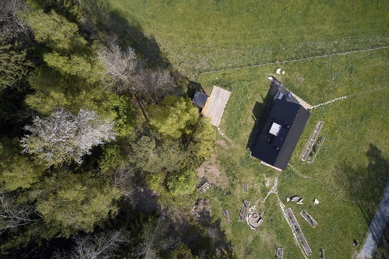Letecký pohled na dům s tmavou střechou vedle lesa a louky