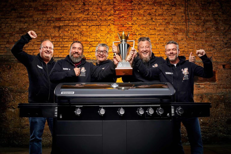 Pět mužů prezentuje plynový gril Tenneker a trofej před cihlovou zdí
