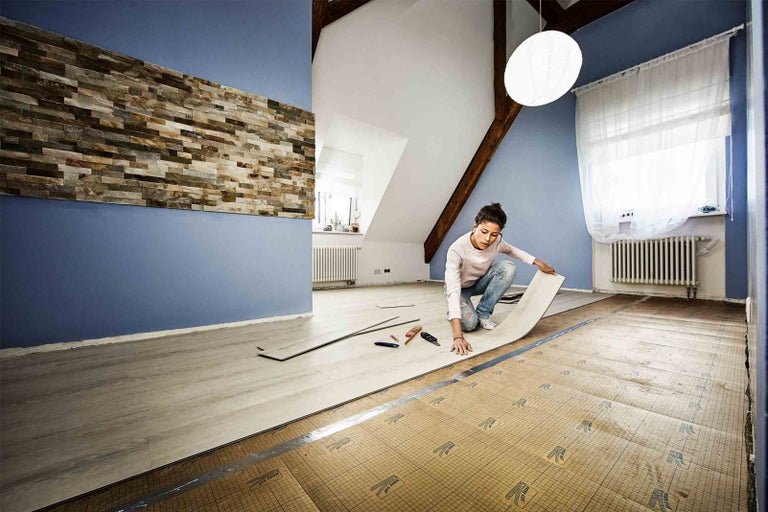 Žena pokládá designovou podlahu v podkrovním pokoji s kamennou stěnou
