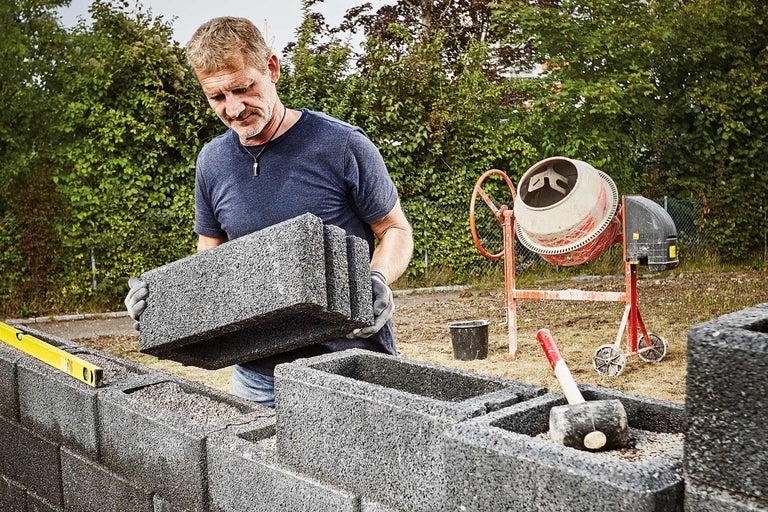 Muž staví zeď z bednicích tvárnic s míchačkou na beton v pozadí