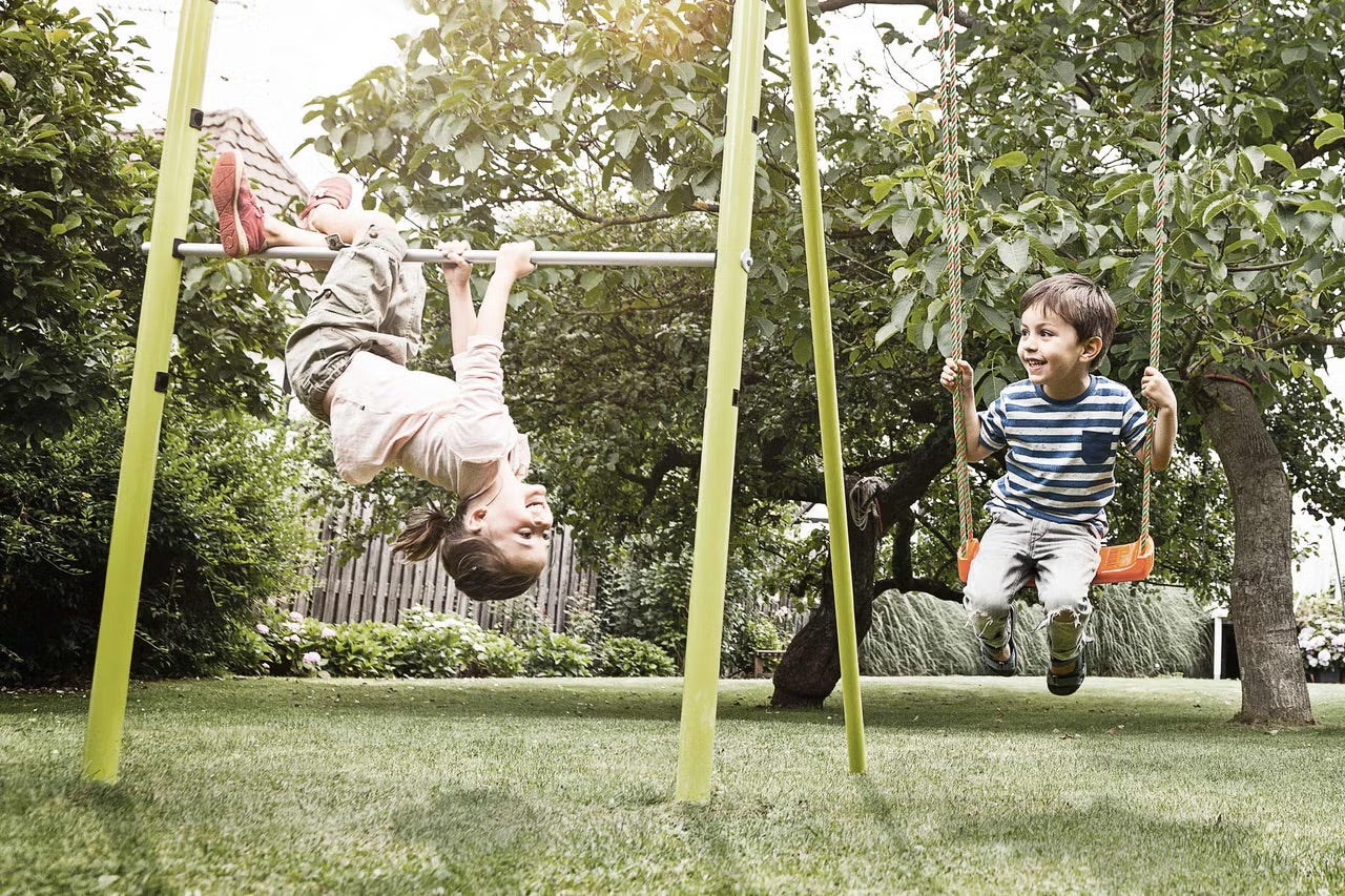 Děti si hrají na hřišti s houpačkou a hrazdou na zahradě.