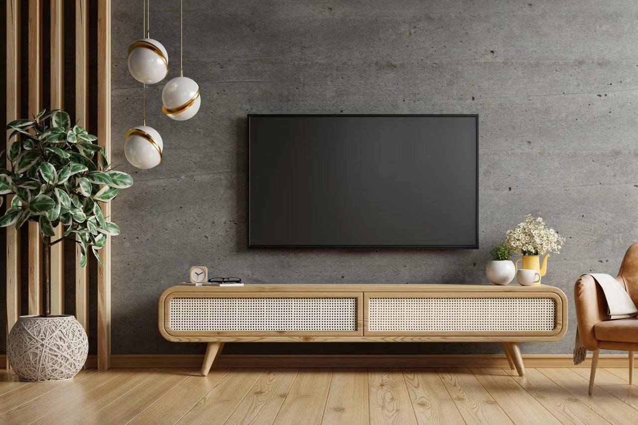 Moderní obývací pokoj s televizí na stěně s betonovým vzhledem, dřevěnou TV skříňkou s výpletem, dřevěnou podlahou a velkou pokojovou rostlinou.