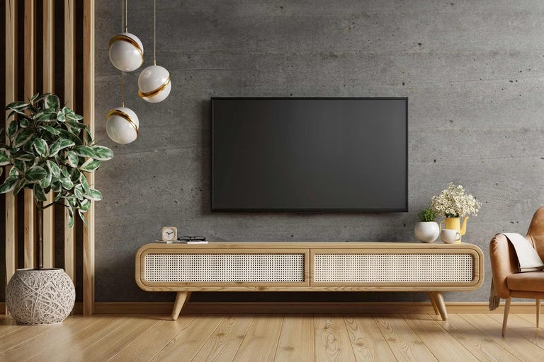 Moderní obývací pokoj s televizí na stěně s betonovým vzhledem, dřevěnou TV skříňkou s výpletem, dřevěnou podlahou a velkou pokojovou rostlinou.