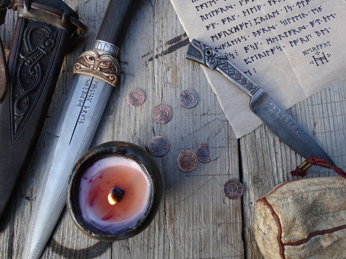 Scéna s motivem Vikingů, včetně dýek, svíčky, mincí a pergamenu na dřevěném pozadí
