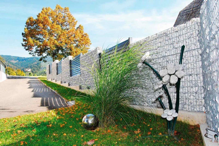 Krajina s gabionovou zdí, okrasnou trávou, kovovou koulí a stromem s podzimním listím