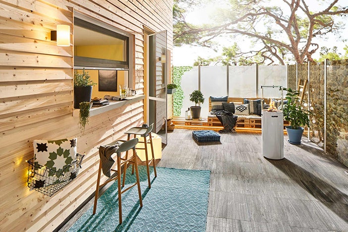 Venkovní prostor s dřevěným obkladem, bar, stoličky, salonek s paletovým nábytkem a plynovým ohřívačem.