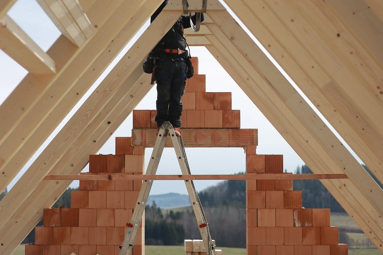 Stavební dělník na žebříku při stavbě domu z dřeva a cihel.
