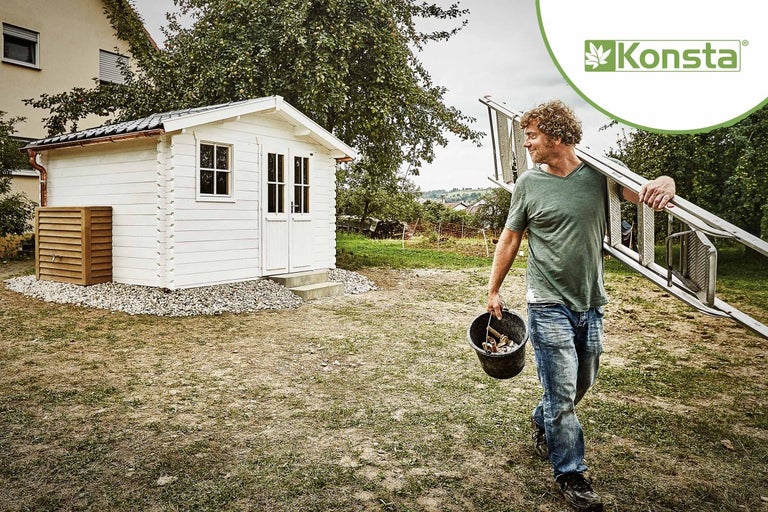 Muž nese žebřík a kbelík poblíž zahradního domku Konsta