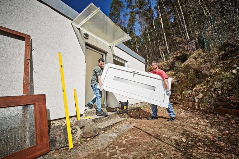 Dva lidé nesou dveře se skleněnou vložkou k domu.